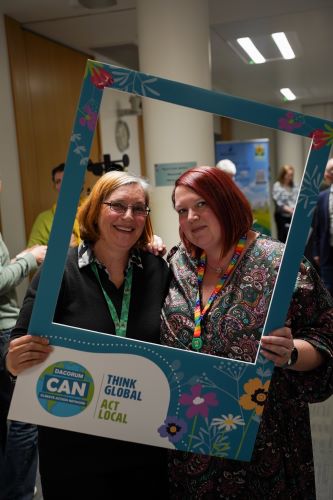 Two women stand behind selfie frame displaying the Dacorum CAN logo.
